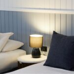 Close-up of twin beds in a Deluxe Queen Room at Settlers Inn Port Macquarie, with white bedding, dark cushions and bedside lamp.