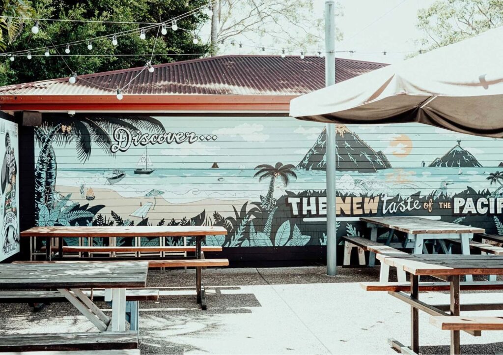 Outdoor beer garden at Settlers Inn Port Macquarie featuring picnic tables, umbrellas, festoon lights and a colourful wall mural.